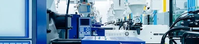 Row of blue and white machines with control panels; hoppers and pipes in a bright hall.