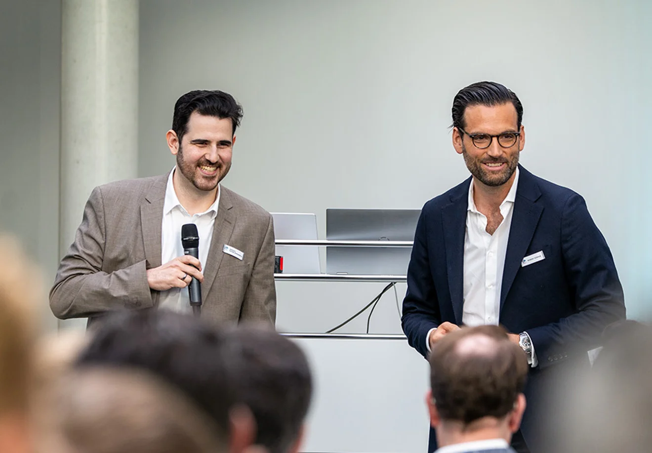 Robert Küpper mit GOB-Mitarbeiter auf Bühne; Moderator mit Mikrofon, beide lächeln ins Publikum.