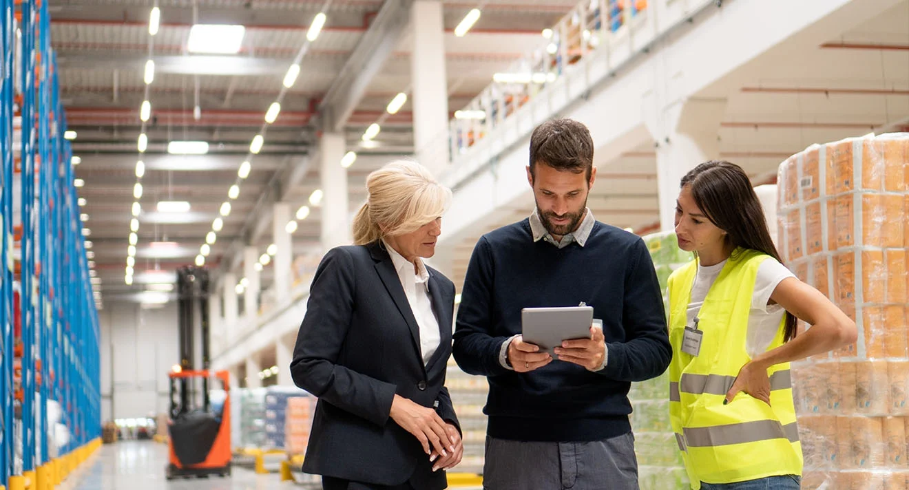 Effiziente Steuerung Ihrer Lagerprozesse – mit ERP-System Was ist ERP? Team überprüft Lagerdaten und Prozesse digital auf einem Tablet in moderner Halle.