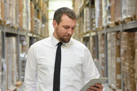 Warehouse manager uses tablet to control warehouse processes via  WMS system in high-bay warehouse