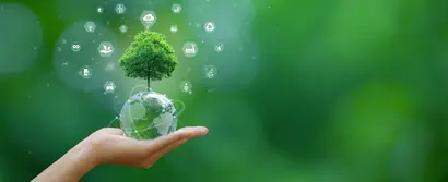 Hand holding a transparent globe with a tree against a green background.