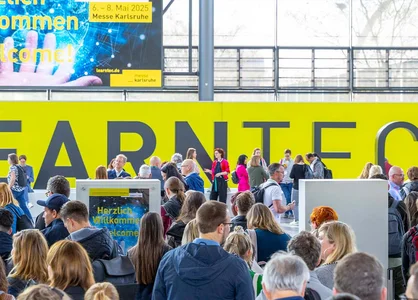 LEARNTEC 2025 in Karlsruhe: Eingang Besucher | 1920 x 780 Pixel Menschenmenge am Eingang der LEARNTEC 2025 in Karlsruhe vor gelber Wand mit Schriftzug