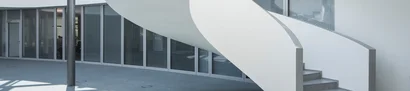 Atrium mit geschwungener weißer Treppe, Glasfronten und grauem Boden im GOB-Gebäude.