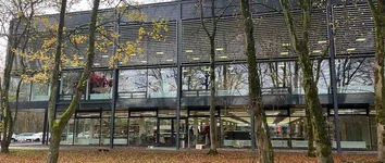 Verglaste Fassade der Blue Box Bochum mit Lamellen; Bäume im Vordergrund, Innenräume sichtbar.