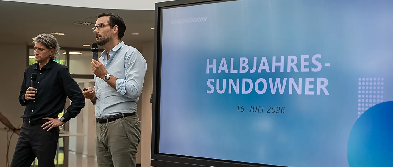 Die GOB-Geschäftsführer Tim Bellen und Robert Küpper sprechen neben der Leinwand zum Halbjahres-Sundowner 2026.