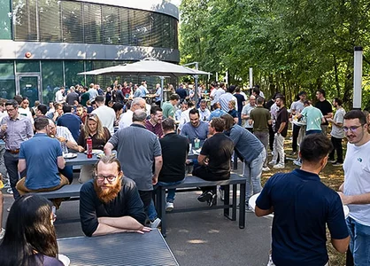 GOB-Mitarbeitende stehen und sitzen beim Halbjahres-Sundowner 2026 an Tischen auf der Terrasse.