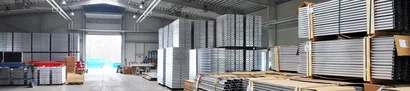 Innenansicht einer Industriehalle: Gestapelte Aluminiumprofile und Paletten vor großem Hallentor