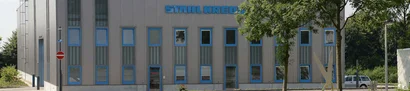Fassade mit blauen Fensterrahmen; Schriftzug STAHL KREBS oben; davor Bäume und Mast