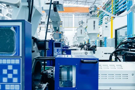 Injection moulding production – machine series in bright production hall Row of blue and white machines with control panels; hoppers and pipes in a bright hall.