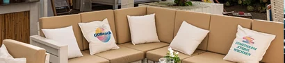 GOB-Sommerevent 2025 – Lounge mit „GOBeach“-Kissen Beige Outdoor-Ecksofa mit Kissen; Aufdrucke „GOBeach“ und „GEMEINSAM STABIL WACHSEN“ sichtbar.