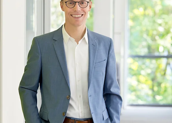 Christoph Hilligen, CEO World Vision Deutschland e. V. Lächelnder Mann mit Brille im blauen Anzug steht in einem hellen Büroflur von World Vision.