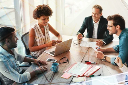 Abläufe Ihrer Kammer digital organisieren und steuern – mit unserer Softwarelösung unitop Symbolbild: Vier Personen am Tisch, eine am Laptop, andere besprechen Unterlagen und Stifte.