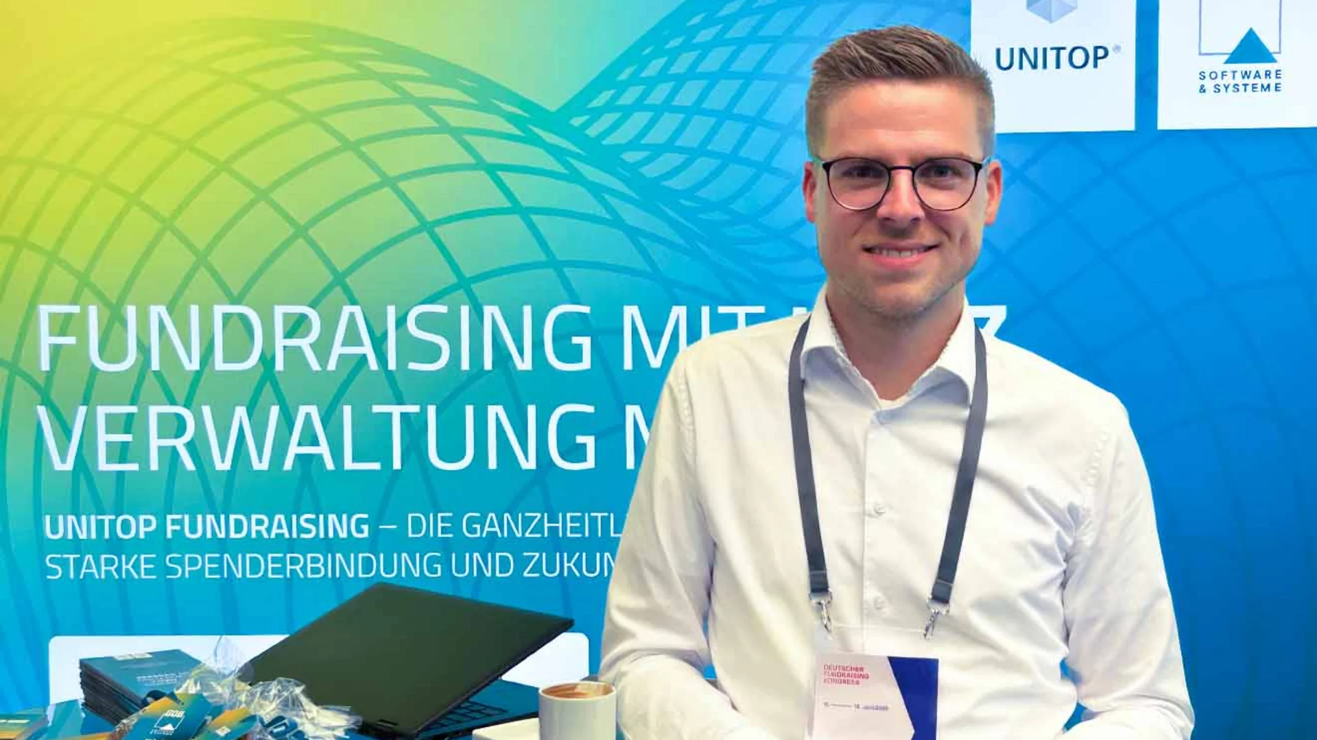 Tim Wagemans am GOB-Stand beim DFK 2025 mit Infomaterial, Give-aways und Kaffee im Vordergrund