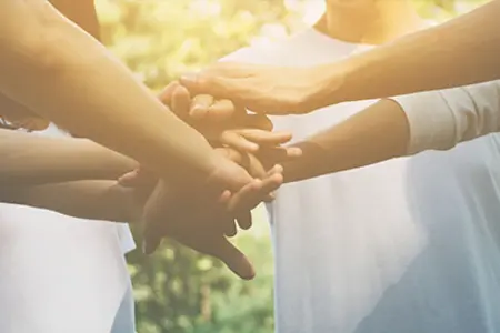 Menschen legen ihre Hände übereinander, symbolhaft für Teamarbeit und Zusammenarbeit.