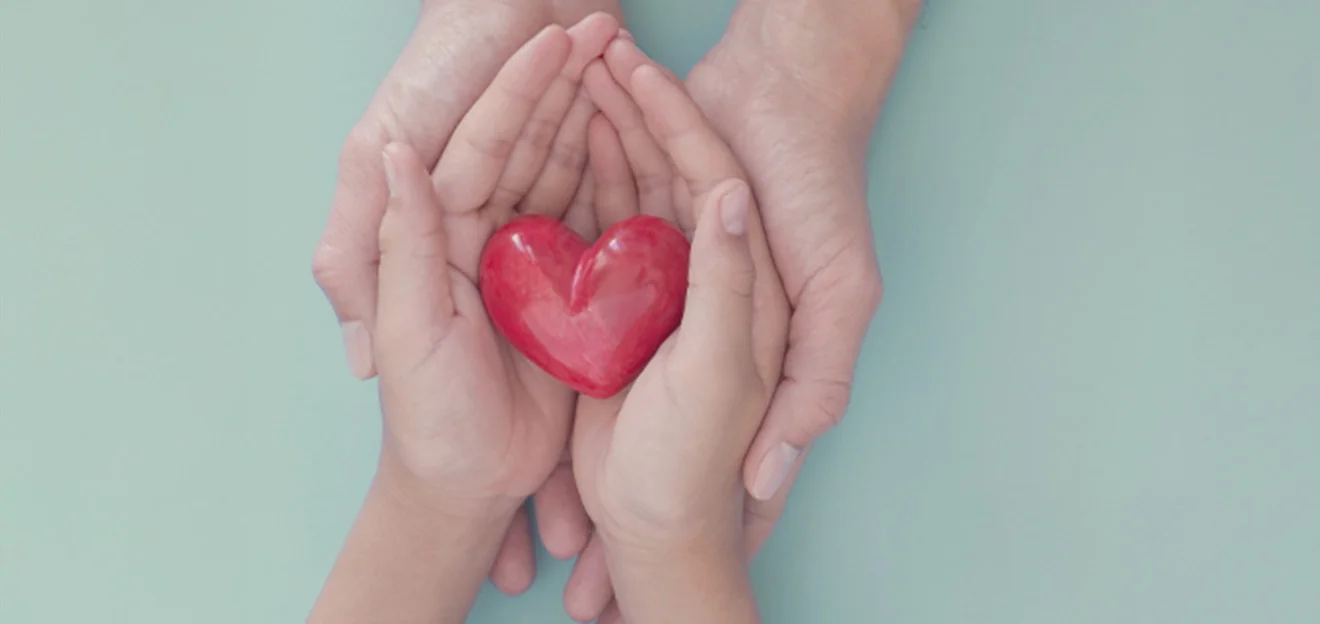 Illustrative image: Adult and child hands hold a red heart against a light background.