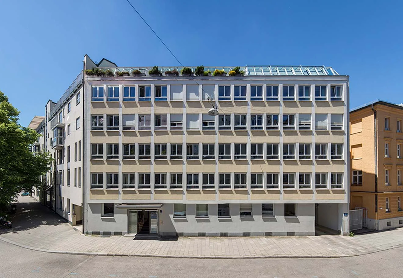 Bürogebäude mit vielen Fenstern, Dachbegrünung und Glasdach unter klarem blauen Himmel.