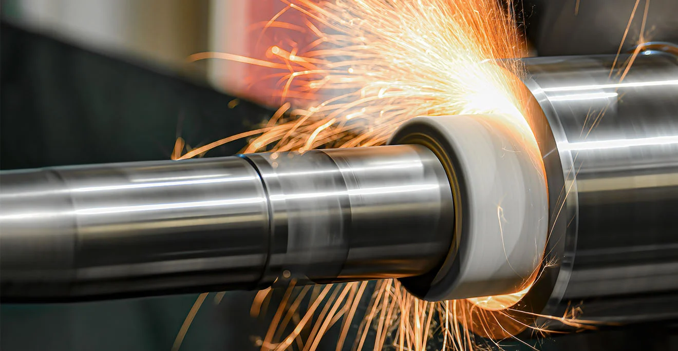 Schleifmaschine bearbeitet eine Metallwelle, Funken sprühen sichtbar an der rotierenden Oberfläche