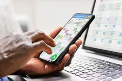 Person gleicht Kalender auf Smartphone mit Kalender auf Laptop ab