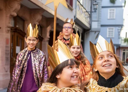Kindermissionswerk ‚Die Sternsinger‘ in Aktion Fünf fröhlich lächelnde Kinder laufen im Sternsinger-Gewand durch eine Altstadt