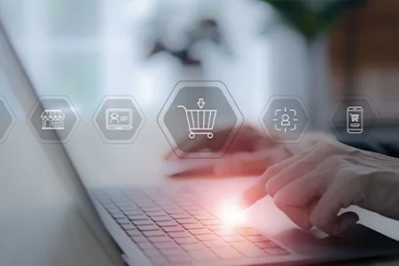 Hände tippen auf Laptop, davor Symbole für Warenkorb, Kunden, Kanäle – Multichannel-E-Commerce.