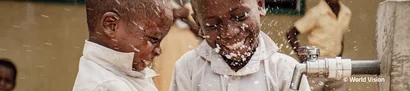 Zwei Kinder lachen, während sie an einem Wasserhahn mit spritzendem Wasser spielen.