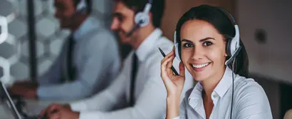 Woman with headset smiling friendly at the camera, two call centre agents working in the background