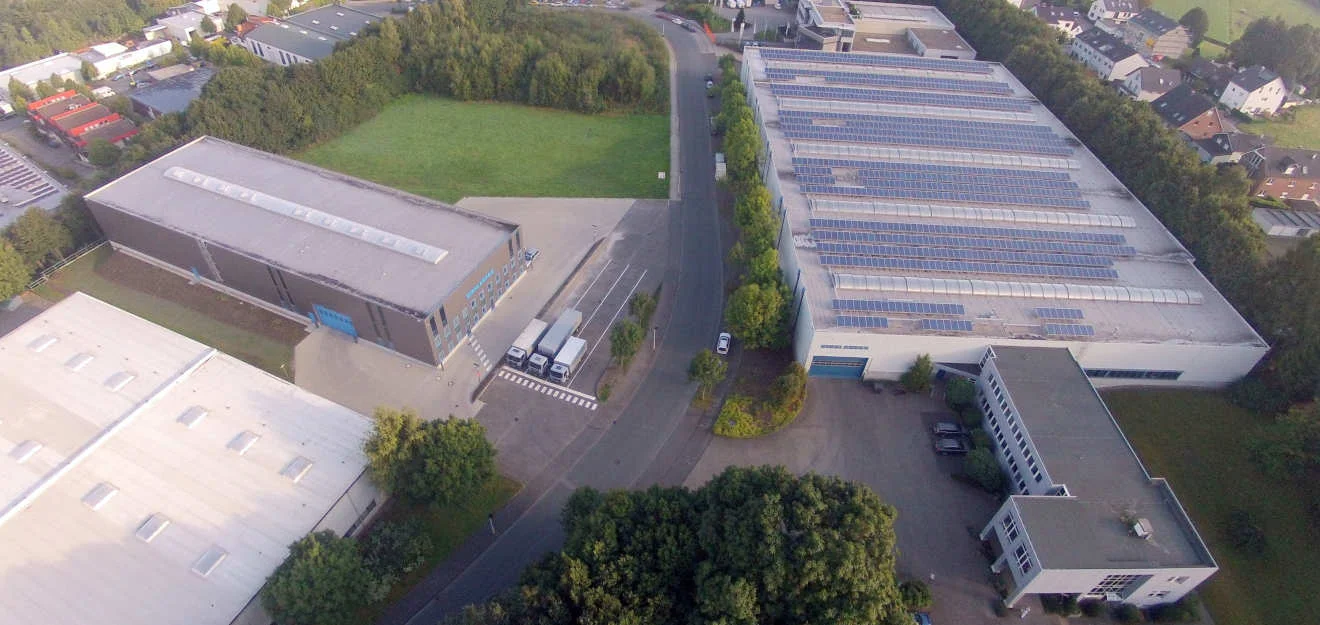 Luftaufnahme eines Werksgeländes; Hallendächer mit Solarmodulen und Zufahrtsstraße