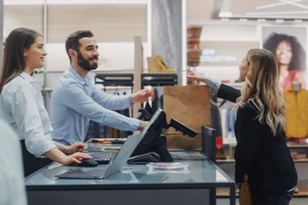 Verkäufer und Verkäuferin übergeben Einkaufstüte an Kundin in moderner Modefiliale.