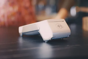 Nahaufnahme eines mobilen Zahlungsterminals mit NFC-Symbol auf einem dunklen Tresen