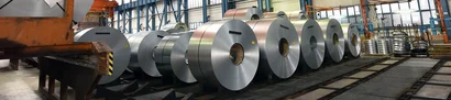 Große Stahl-Coils stehen aufgereiht in einer Produktionshalle mit Krananlage und Lagerbereichen