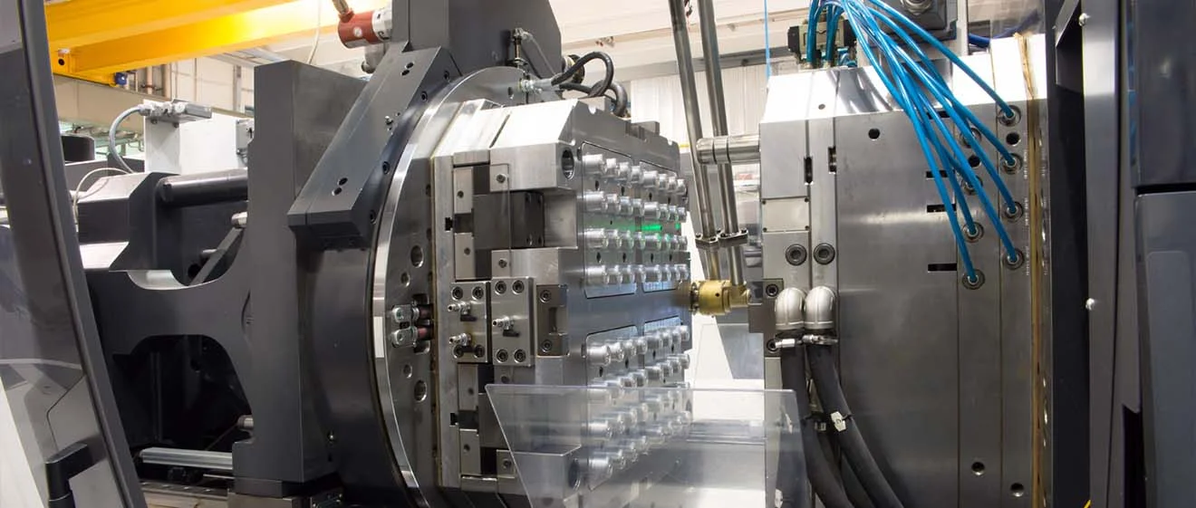 Close-up of a large moulding tool on a machine; blue hoses and transparent box.