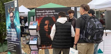 Mehrere Besucher stehen am GOB-Stand vor Posterwand; daneben Prospektständer mit Flyern.