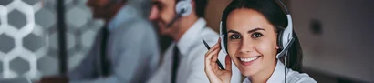 Exklusive Leistungen für Kunden – mit dedizierten Ansprechpartnern Frau mit Headset lächelt freundlich in die Kamera, zwei Call Center Agents arbeiten im Hintergrund