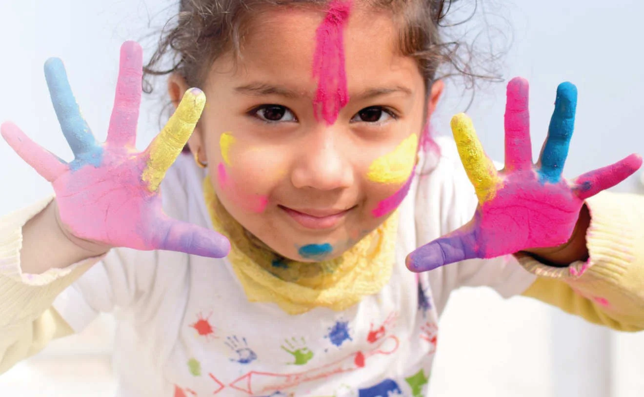 Kind mit bunter Farbe auf Händen und im Gesicht lächelt bei der Deutschen Kinderkrebsstiftung.