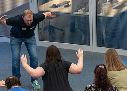 Teilnehmende machen eine Bewegungsübung im Raum, angeleitet von einem Trainer.