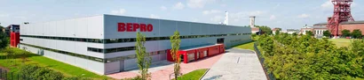 BEPRO-Unternehmenssitz – Außenansicht mit Logo Graues Firmengebäude mit rotem BEPRO-Schriftzug; vorn Weg und Bäume, rechts Industrieanlage