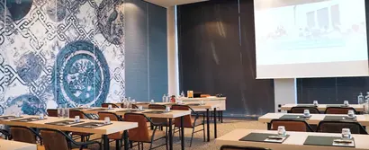 GOB-Meeting 2024 im Konferenzraum des Van der Valk Hotels Düsseldorf Modern eingerichteter Konferenzraum mit Tischen, Stühlen und kunstvoller Wanddekoration.