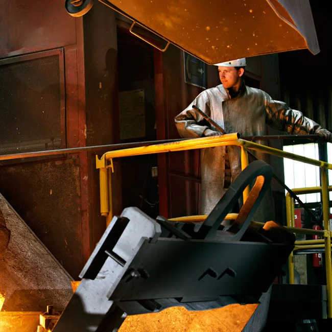 Working on the melt in the foundry | Stahlwerke Bochum Foundry worker in protective coat at railing; liquid metal glows from a ladle below