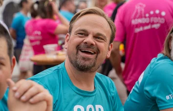 Ein GOB-Mitarbeiter mit Bart lacht herzlich in die Kamera, umgeben von Laufteam und Festivalstimmung