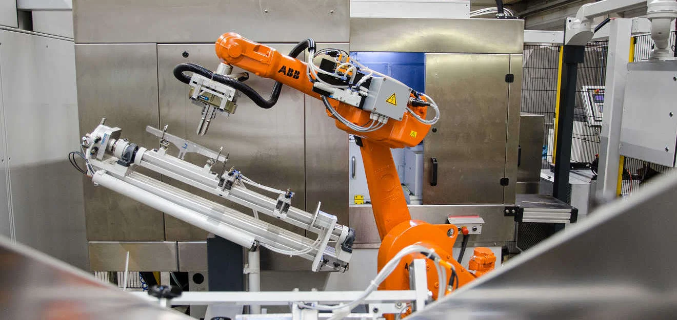 Automatisierte Fertigung mit Industrieroboter in der Produktion von Winterhoff Picard Orangener Industrieroboter arbeitet in automatisierter Fertigungsanlage von Winterhoff Picard.