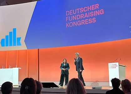 Deutscher Fundraising Kongress 2025: Eröffnungsbühne | 1905 x 425 Pixel Eröffnungsbühne des DFK 2025 mit Vortragenden vor Publikum und großem Veranstaltungsbildschirm