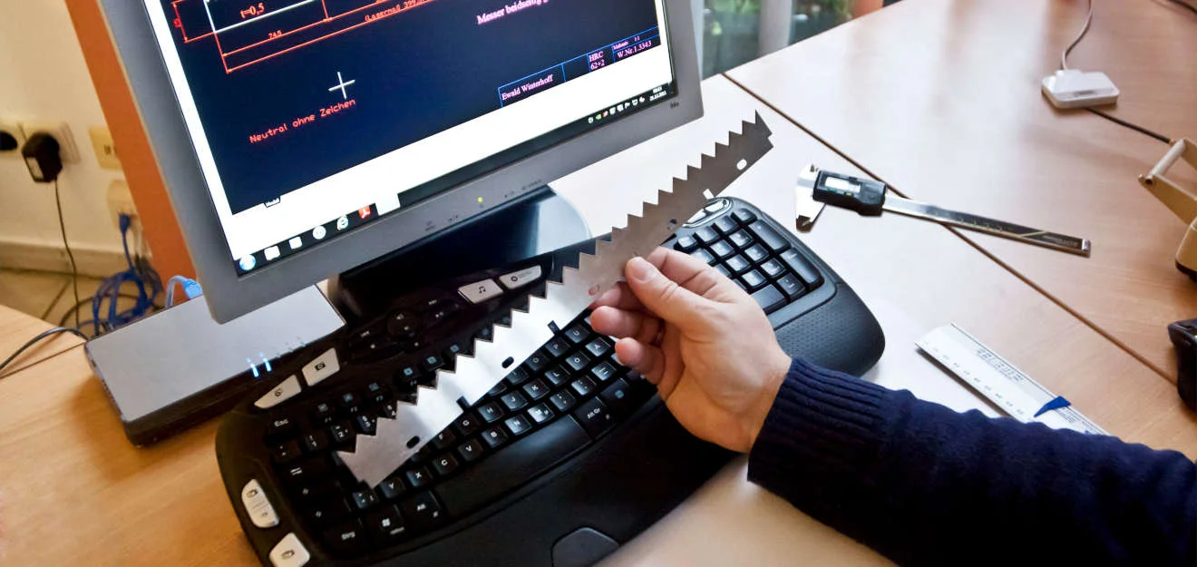 Konstruktion und Vermessung eines Maschinenmessers am CAD-Arbeitsplatz von Winterhoff Picard Hand hält Maschinenmesser über Tastatur, auf dem Bildschirm CAD-Zeichnung bei Winterhoff Picard.