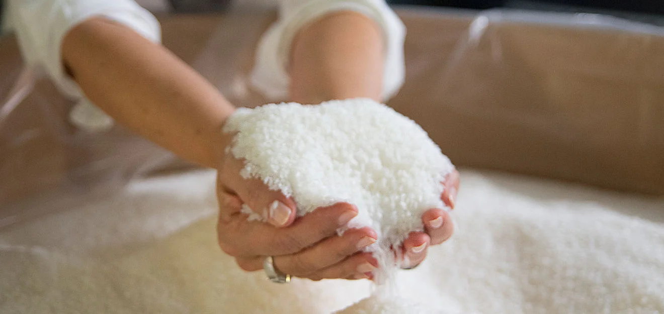 Zwei Hände halten eine Portion weißes Granulat; im Vordergrund rieselt es durch die Finger