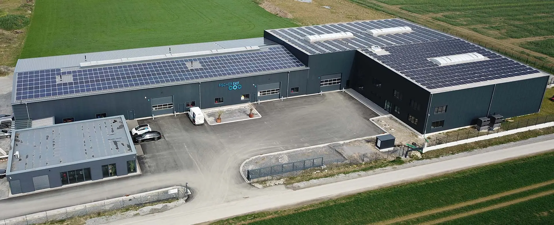 Luftaufnahme Fischer-EKF-Firmengebäude mit Solaranlagen auf dem Dach & Parkplatz umgeben von Feldern