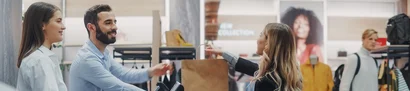 Retail – shopping with personal advice at the checkout Sales assistant hands shopping bag to customer in modern fashion store.