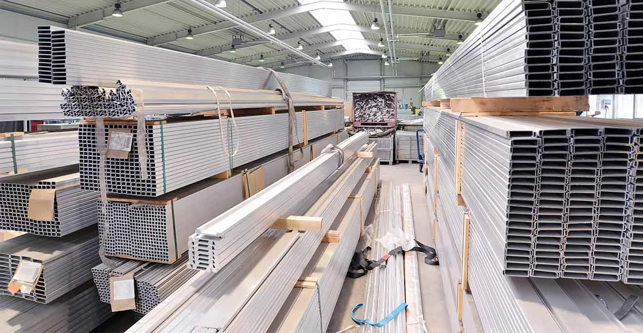 Aluminium- und Hohlkammerprofile liegen in Stapeln sortiert in einer hellen, modernen Lagerhalle.
