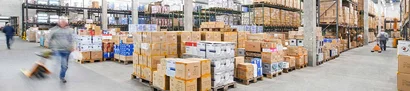 Logistik-Halle von Gerd van Well mit hochgestapelten Geschirrkartons und zwei Lagermitarbeitern