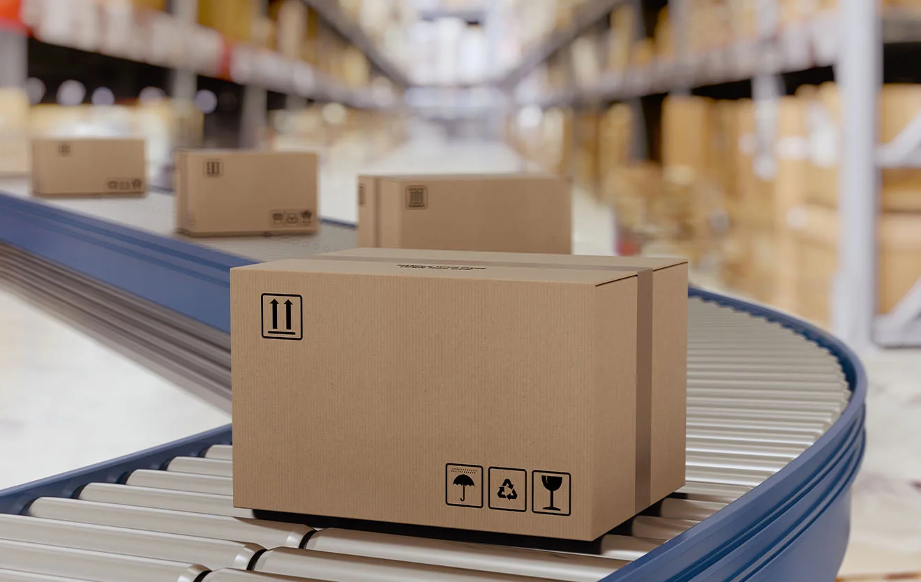 Cardboard packages travel on a conveyor belt through a storage area with shelves.