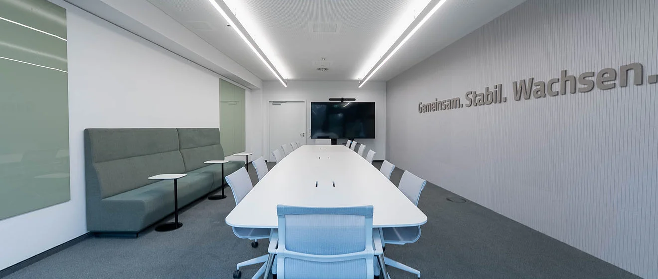 „Gemeinsam. Stabil. Wachsen.“ – neuer Schulungsraum in der GOB Schulungsraum bei GOB mit langem Tisch, Screen und Motto „Gemeinsam. Stabil. Wachsen.“