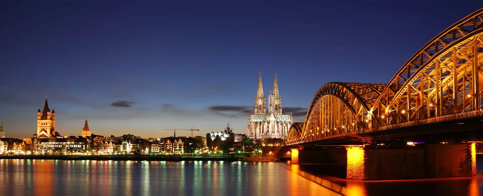 Kölner Panorama bei Abenddämmerung mit beleuchteter Hohenzollernbrücke und Kölner Dom.